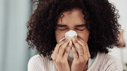 A woman blows her nose with a tissue, which could be a sign of cold or allergies