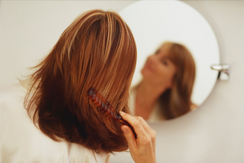 women running a comb through her hair as she looks in the mirror