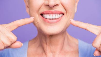 foods for healthy gums: Concept of having strong healthy straight white perfect teeth at old age. Cropped portrait of beaming smile female pensioner pointing on her teeth, isolated over violet background