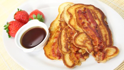 A stack of bacon pancakes with a side of maple syrup and strawberries