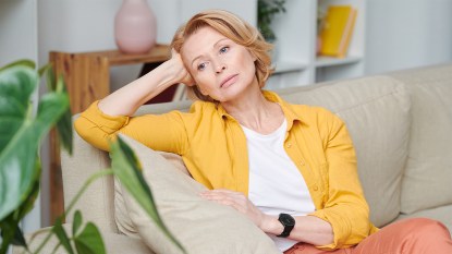 Sad woman sitting alone on couch with her head resting in her hand
