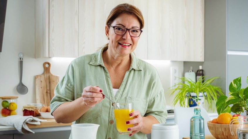 A woman smiling as she stirs creatine into her glass of orange juice in her kitchen