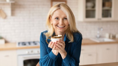 A blonde woman in a blue top holding a cup of tea for bloating