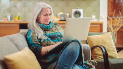 best jobs for women over 50 are things you can do at home, like this lady is doing on her couch.
