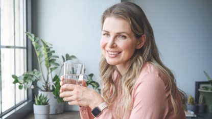 A woman in a pink shirt holding a glass of water to stop burning stomach pain