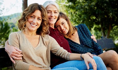 Woman sitting outside on bench with her two adult daughters