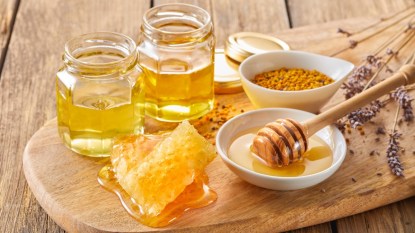 A wood board with jars of honey and fresh honeycomb, which are gut-friendly sweeteners