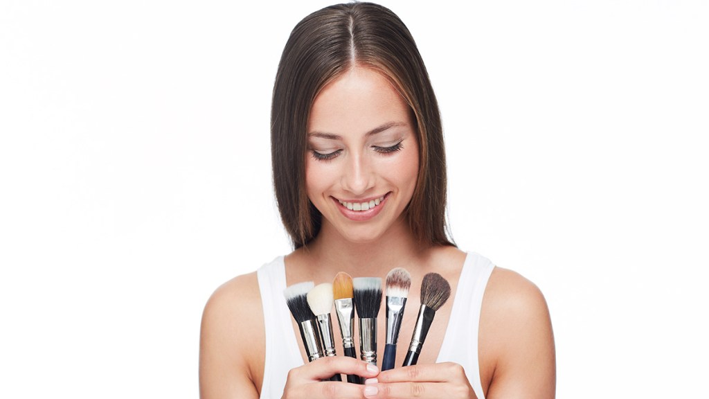 Brunette woman holding a variety of makeup brushes