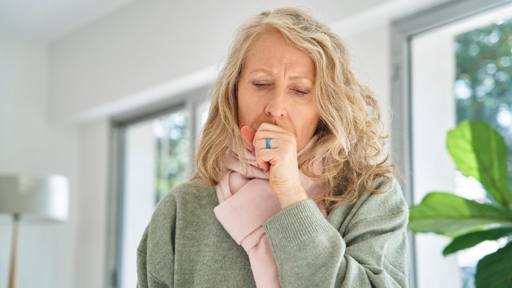 A woman with blonde hair and a scarf coughing