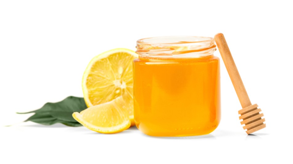 A jar of honey next to a sliced-open lemon, which can be used to soothe a cough
