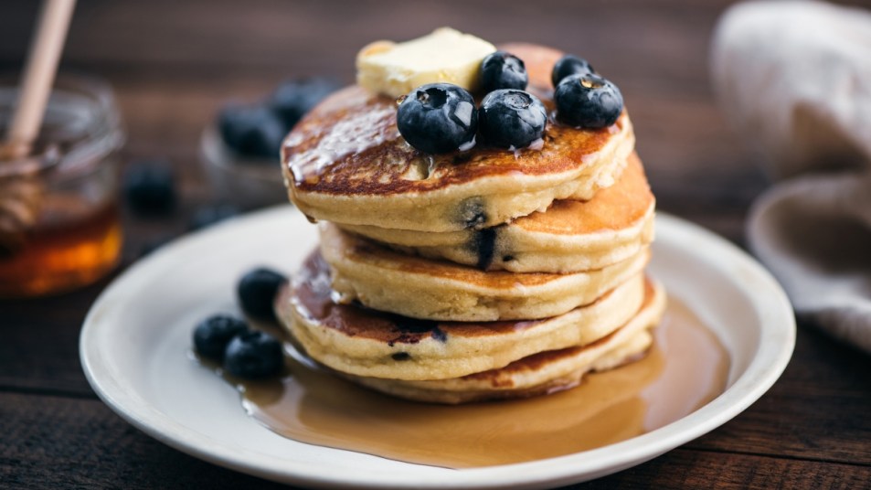 fluffy pancakes on a white plate with syrup and blueberries