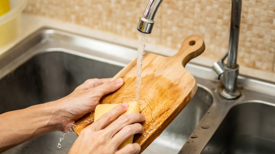 Woman cleaning wooden cutting board with a sponge at the kitchen sink