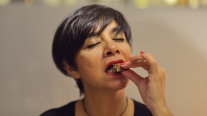 mature woman with cropped hair taking a bite of chocolate, savoring it, eyes closed