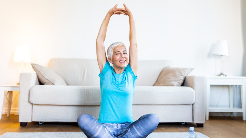 A woman in fitness attire seated on the floor reaching her arms upward while practicing yoga for menopause