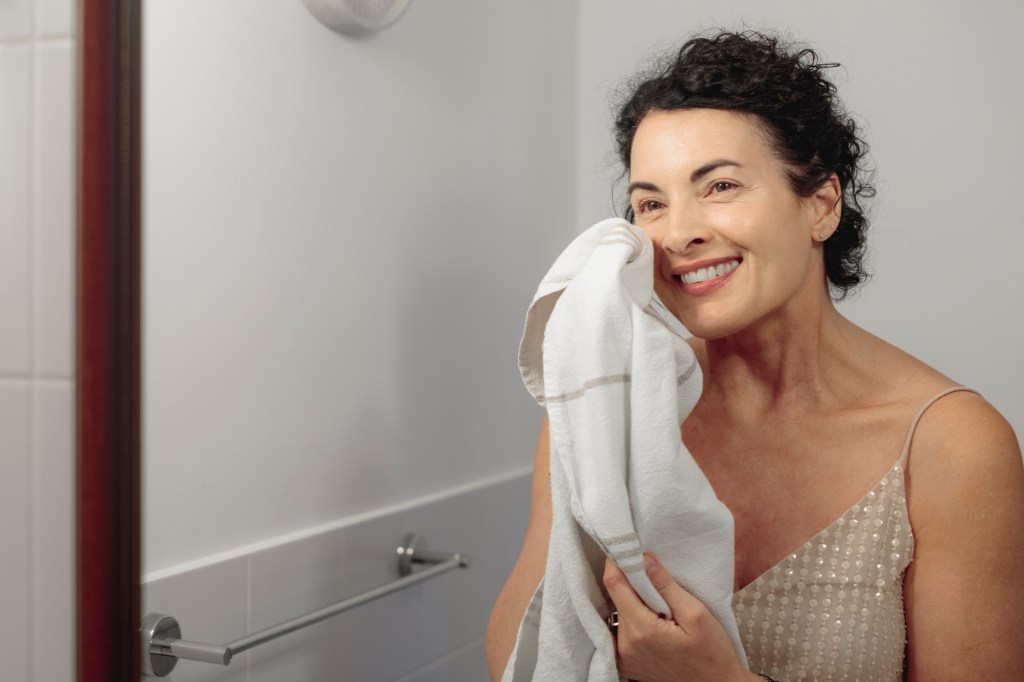 mature woman smiling in mirror after washing face.