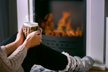 Woman sitting in front of the fireplace and holding cup of tea in hand on legs