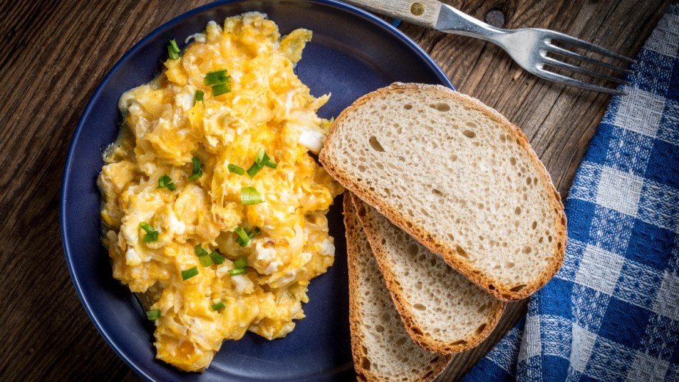 Scrambled eggs with onion and chives served with bread on a blue plate. Top view.