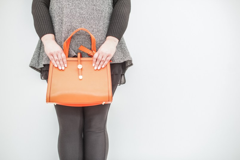 woman in a sweater dress and leggings holding an orange purse