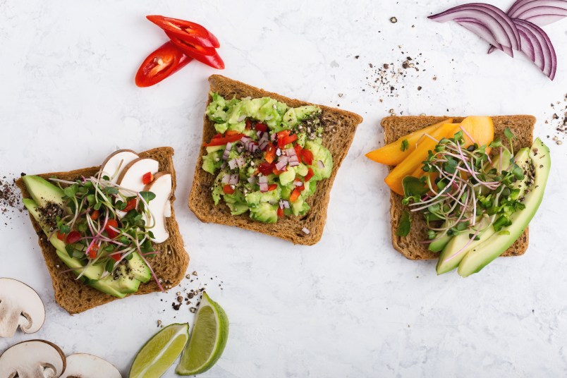 Variety of avocado toasts with fresh radish cress, mushrooms and persimmon. Plant based colorful vegan snack on gray background viewed from above