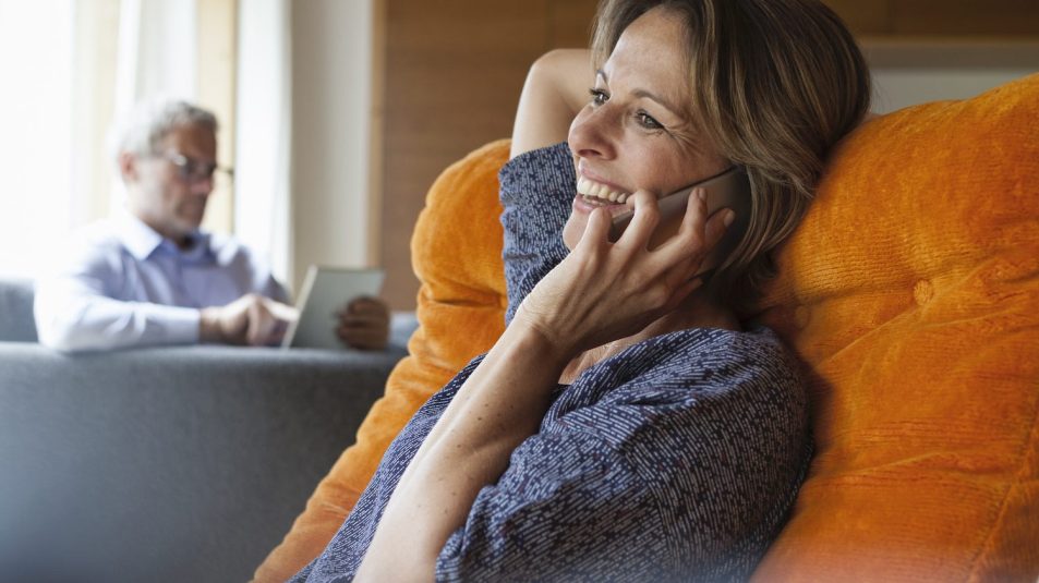 Smiling woman at home on cell phone with husband in background