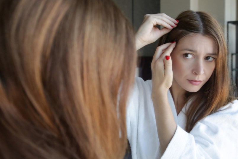 redhead woman examining hair near her scalp in a mirror