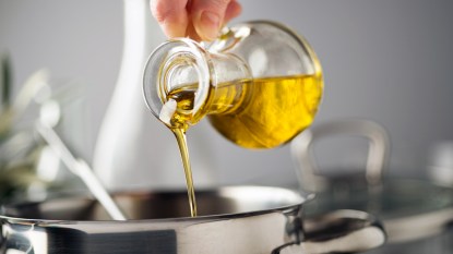 Hand pouring olive oil into pan