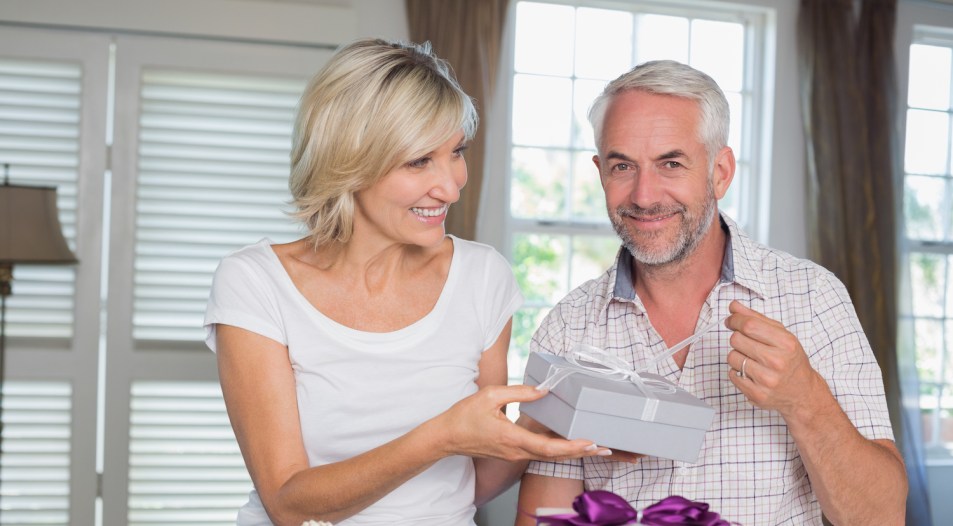 Happy woman giving a gift box to smiling mature man at home