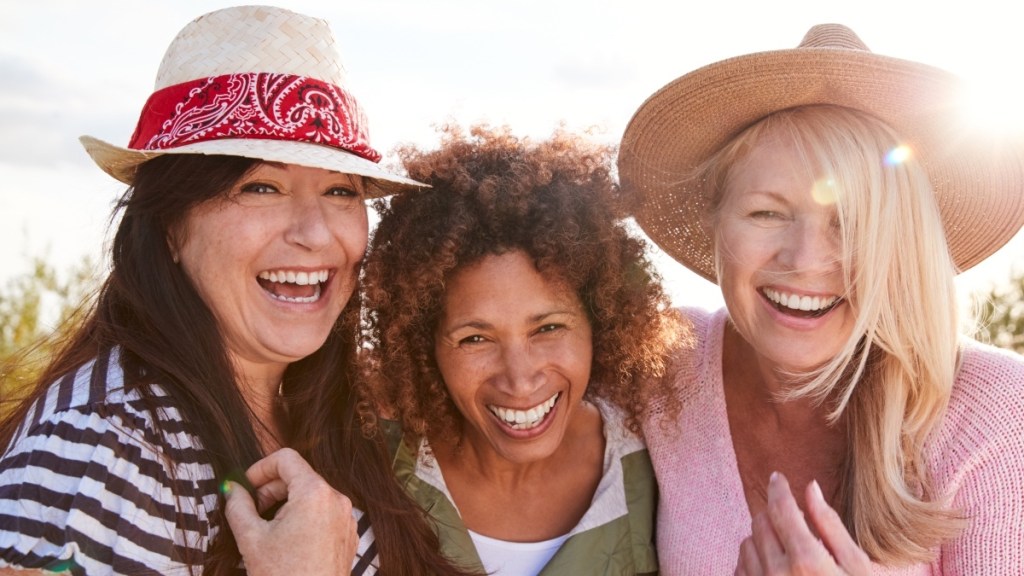 Three women smiling and laughing with their arms around each other enjoying their friendship