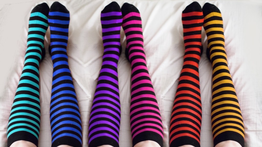 Three women's legs on white sheets wearing colorful striped compression socks for varicose veins