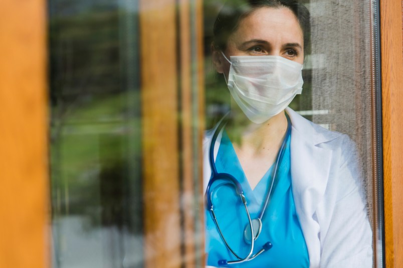 Female doctor looking through window at hospital with face mask on
