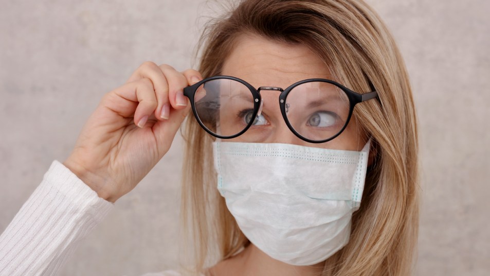 Woman lifting eye glasses while wearing a face mask