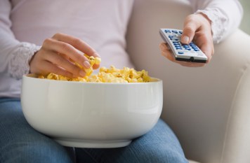 Close up of woman with remote control and bowl of popcorn