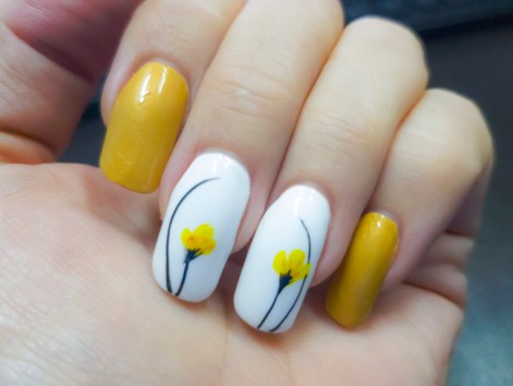 Photo shows lovely spring nail art in the form of white nails with yellow flowers painted on them.