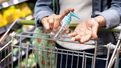 Shopper disinfecting hands with sanitizer in supermarket during shopping