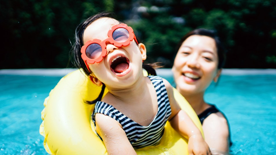 Toddler in sunglasses smiling with mom in pool