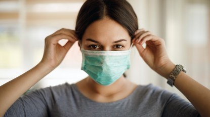 Woman with brown hair putting on a surgical face mask