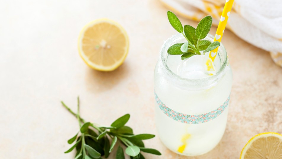 Glass jar of lemonade with sage sprigs and yellow paper straw