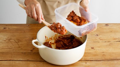 Hands putting leftover meat sauce in Tupperware