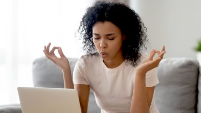 Stressed woman taking a deep breath with her laptop next to her