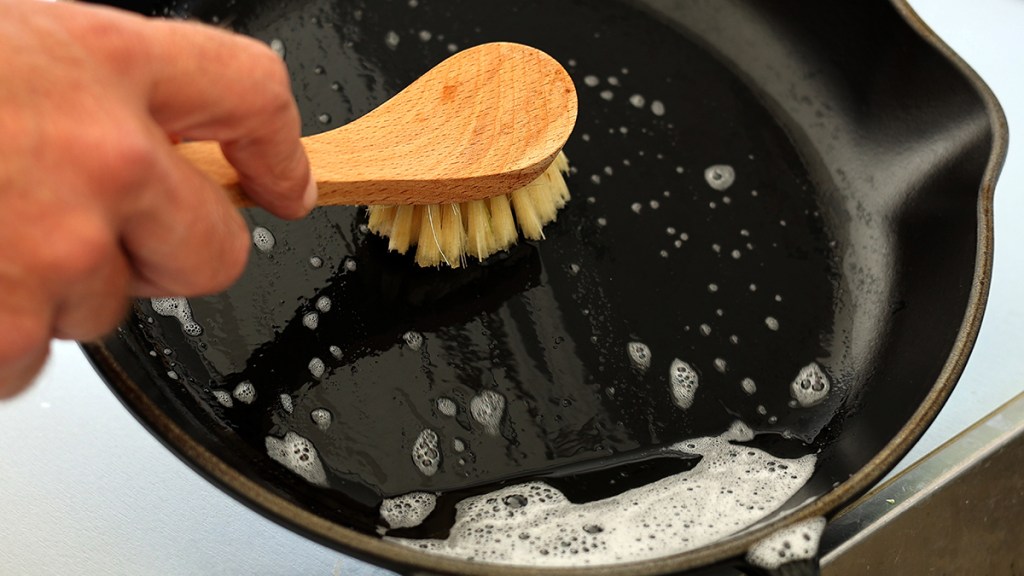 Using soap and a scrub brush on a cast iron pan