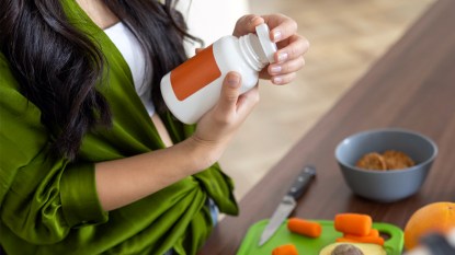 Woman cutting vegetables and holding bottle of supplements