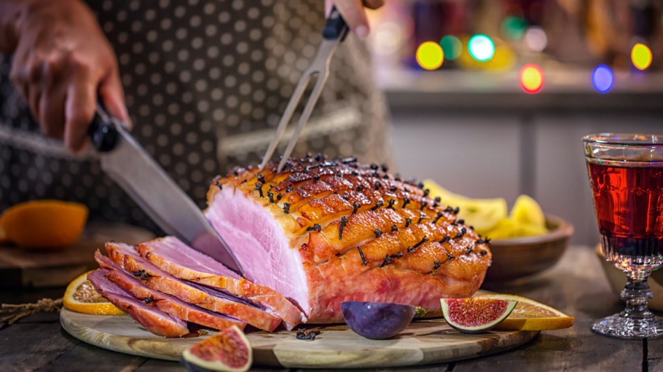 Woman's hands carving baked ham