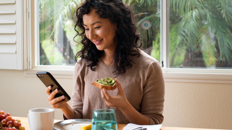 Woman eating avocado toast and looking at her phone