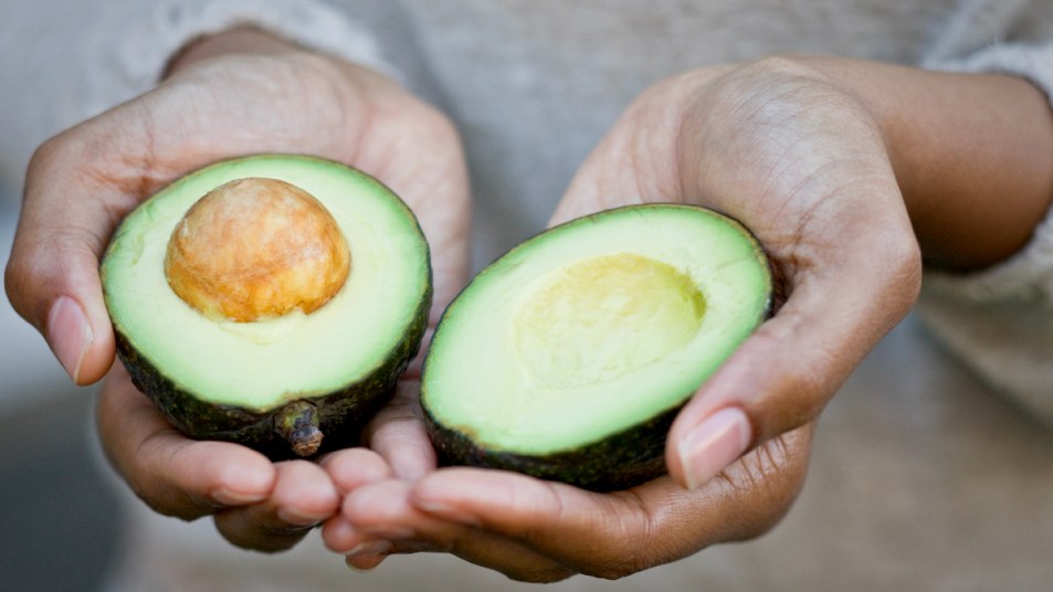 Hands holding a halved avocado