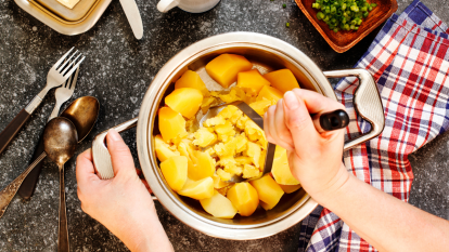 close up of woman's hands mashing potatoes in a metal bowl
