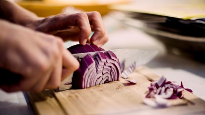 Hands with knife chopping red onion