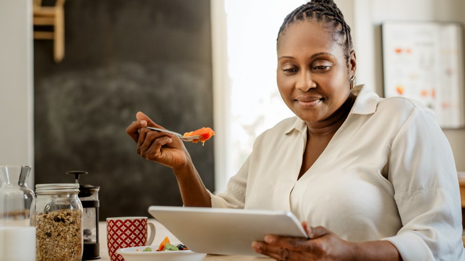 Woman eating and reading a tablet