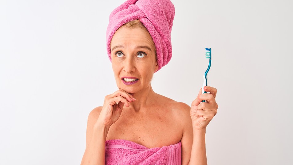 A woman with a toothbrush in her hand wondering if she's brushing too hard