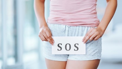 A close-up of a woman holding an SOS sign over her vagina, which can an unbalanced pH