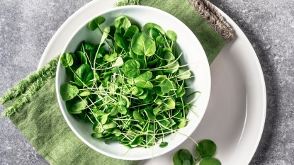 A bowl of watercress, which has many health benefits, on a white plate with a green napkin